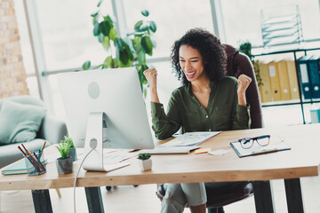 Smiling businesswoman celebrating success at her desk in a modern office filled with natural light...