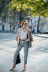 A woman in clothes and glasses walks through the streets of the city