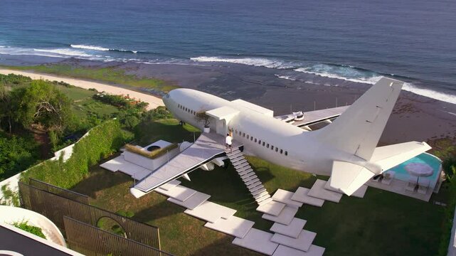Luxury hotel made from airplane in Bali, beachfront villa with ocean view. People walk up the stairs leading into the aircraft. Honeymoon vacation of couple