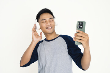 happy Asian young man wearing casual clothing listens to music on headphones while holding a...