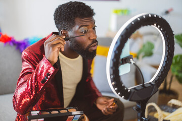 Young non-binary person wearing red blazer and applying make up at home