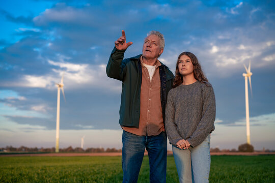 Grandfather and granddaughter in a field with wind turbines discussing renewable energy
