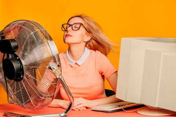 Businesswoman cooling off with a fan at her desk with a vintage computer