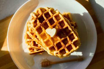 Delicious waffles stacked on a white plate with a small pat of butter melting on top. Honey...