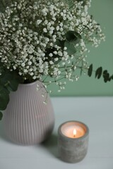 Beautiful gypsophila flowers and eucalyptus branches in vase on white table against turquoise background