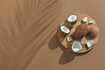 Fresh coconuts and shadow cast by tropical palm on beige background, top view. Space for text