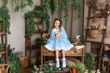 Young girl in blue dress is playing with Easter bunny. A child holds a real rabbit in his arms...