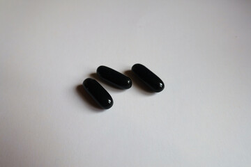 Close view of three black softgel capsules of activated charcoal