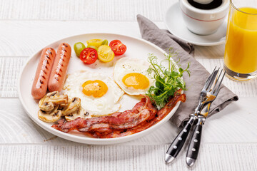 A classic breakfast plate featuring sunny-side-up eggs, crispy bacon, sausages, and fresh tomatoes
