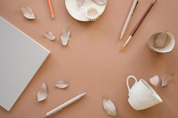 Overhead view of home office desk with a note pad, pens, pencils, a ceramic cup and decorative dried leaves on a table