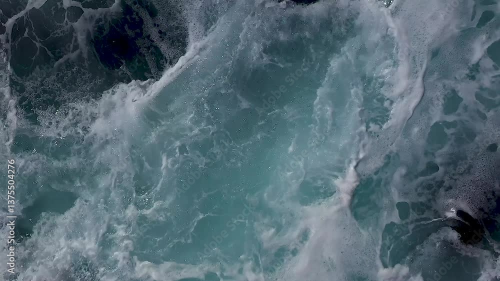 Poster swirling ocean surface seen from directly overhead, showing textured movement of foam and deep aqua 