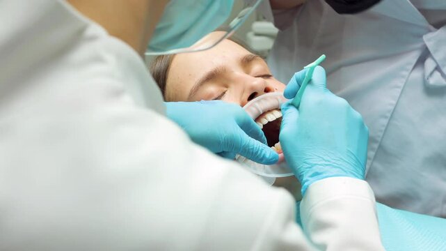 A dentist applies dental adhesive to a teenage patient's teeth using a precision applicator as part of the preparation process for aligner placement during an orthodontic procedure in a modern dental