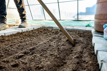 Gardener leveling soil with rake for spring planting of vegetables.