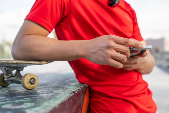 Concept of relaxation and leisure, as the man is taking a break from skateboarding to check his phone