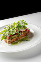 A delicious avocado toast topped with fresh tomatoes, mozzarella, and arugula, sprinkled with grated cheese, served on a white plate.