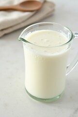 Glass pitcher filled with fresh milk on a smooth white marble surface