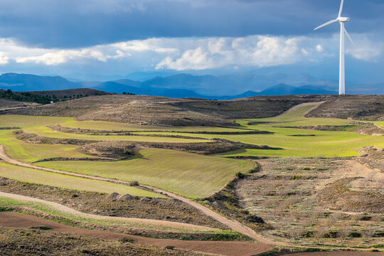 Wide view of renewable energy turbines in Zaragoza, integrated in rolling green landscape and layered with vibrant blue and earth tones