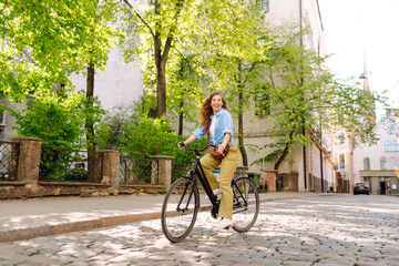 Beautiful woman in casual clothes rides a bicycle along sunny city streets. Concept of walks,...