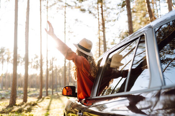 Portrait of a young woman with curly hair enjoying the sunset from the car window. Happy traveler...