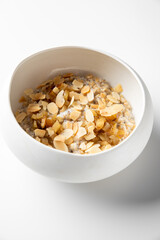 A white bowl filled with oatmeal topped with sliced almonds and dried fruit, showcasing a healthy breakfast option on a light background.
