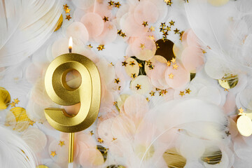 Ninth Birthday Celebration with Gold Candle and Confetti. Golden numeral nine birthday candle lit...