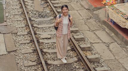 Young woman standing on railway tracks in a bustling market area during daytime in an Asian city