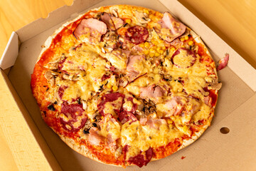 Delicious pizza with ham, pepperoni, and vegetables in a box