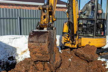 Mini excavator on the construction site. Land work in winter or spring