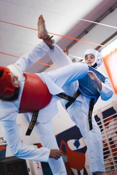 A female martial artist in white gear and blue chest protector lands a kick on the red chest guard of her male opponent during taekwondo sparring on a blue and red mat
