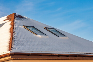 A rooftop laden with fresh snow and two skylights glistens under a clear winter sky.