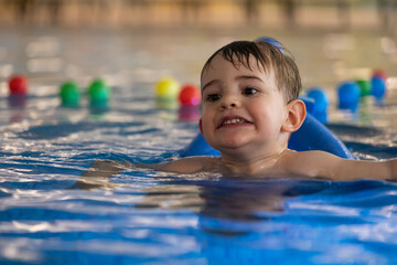 Happy child swimming and playing in indoor pool with colorful balls