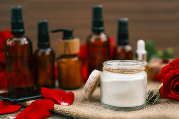 Glass jar with bath salt surrounded by rose petals and amber cosmetic bottles. Natural spa skincare...