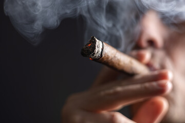 A man smokes a cigar on dark background