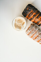 Top view of a sweet pastry coated in coconut flakes next to a glass of cappuccino on a white...
