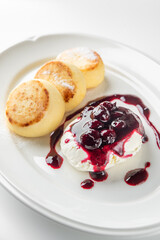 Delicious plate of cheese pancakes served with a dollop of cream and berry sauce. A delightful dessert or breakfast option, garnished and ready to enjoy.