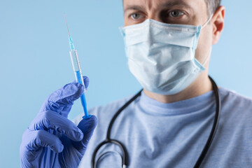A doctor wearing a mask and gloves measures out the vaccine before administering an injection