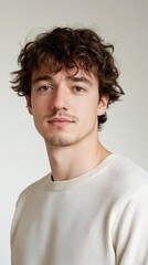 Fototapeta premium Portrait of a Young Man with Curly Hair Wearing a Cream-Colored Sweatshirt