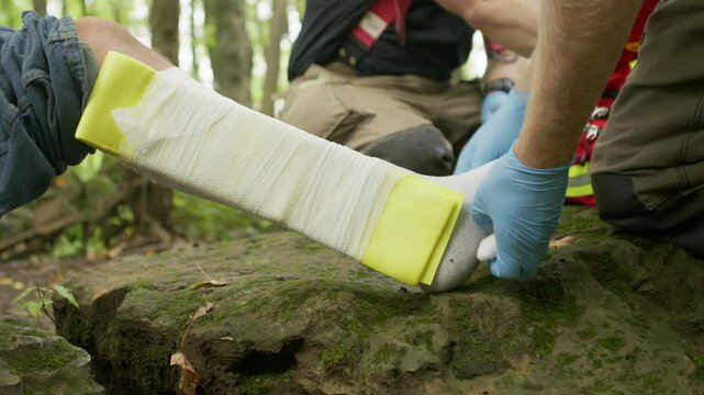 A first responder wraps a broken foot with a splint in the woods.