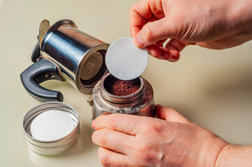 Hands preparing an Italian moka pot with a paper filter for a rich coffee experience.