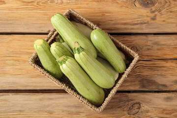 Wicker box with fresh green zucchini on wooden background