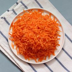 Grated carrots on white plate resting on striped towel, view from above