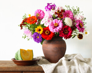 Colorful bouquet of garden flowers in clay vase with pumpkin slice on rustic wooden table