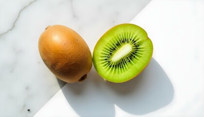 A high-angle, close-up shot captures a whole kiwi and a halved kiwi, positioned on a surface that transitions from a marble-like pattern to a solid white