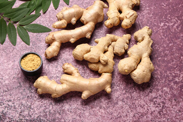 Fresh ginger roots with leaves and bowl of dried powder on purple background