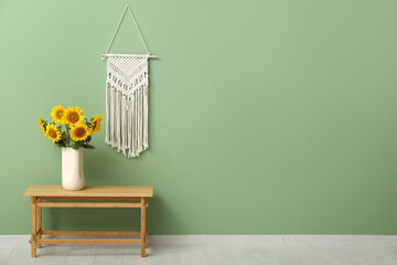 Vase with beautiful sunflowers on table and decor hanging on green wall in room