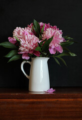 Pink peonies blooming in white pitcher on wooden table