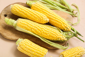 Wooden board with fresh corn cobs on beige table