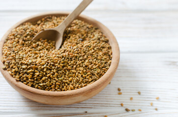 Dry fenugreek or shambhala in a wooden bowl with a spoon on the table. Medicinal plant from the Middle East. Alternative medicine concept. Selective focus. Copy space. Horizontal orientation