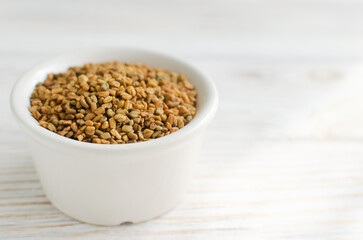 Dry fenugreek or shambhala in a bowl on a white wooden table. Medicinal plant from the Middle East. Alternative medicine concept. Selective focus. Copy space. Horizontal orientation