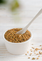 Dry fenugreek or shambhala in a bowl with a spoon on a white wooden table. Medicinal plant from the Middle East. Alternative medicine concept. Selective focus. Vertical orientation